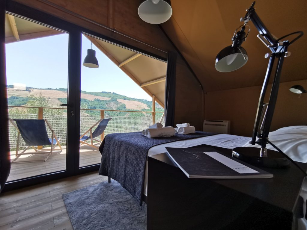 interno di una lodge con letto matrimoniale, terrazzo con due sdraio con vista sulle colline abruzzesi