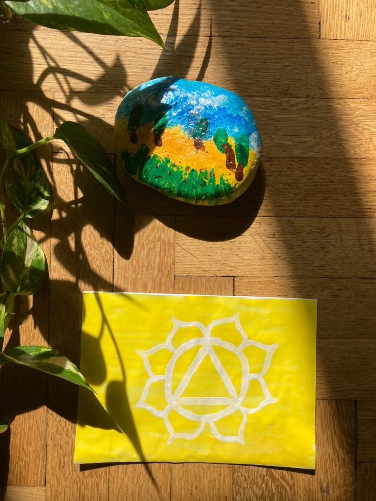 foglio giallo con simbolo terzo chakra appoggiato su parquet illuminato dal sole vicino ad una pianta