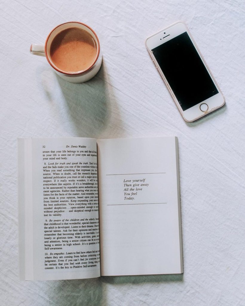 flatlay con libro aperto, i phone bianco e tazza di caffè latte su sfondo bianco